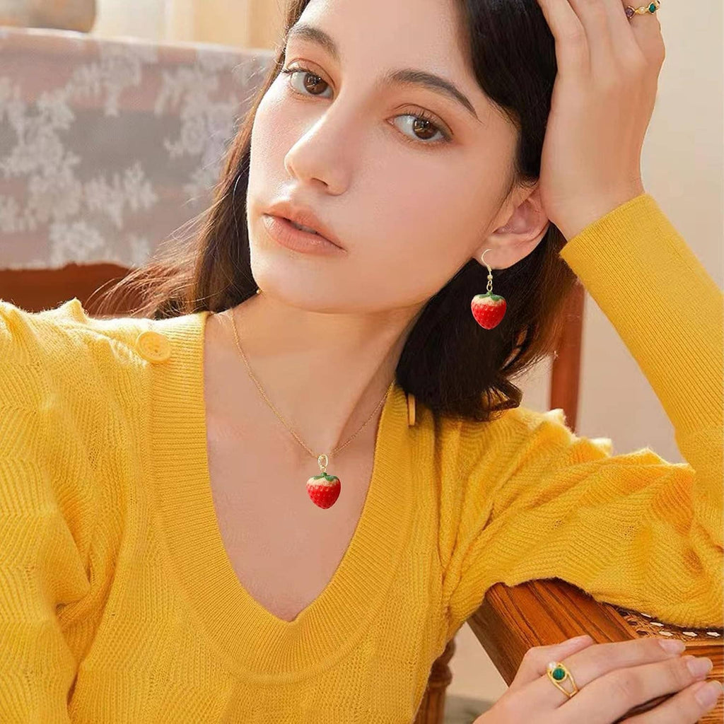 Gold-tone strawberry pendant necklace with red strawberry dangle earrings on woman