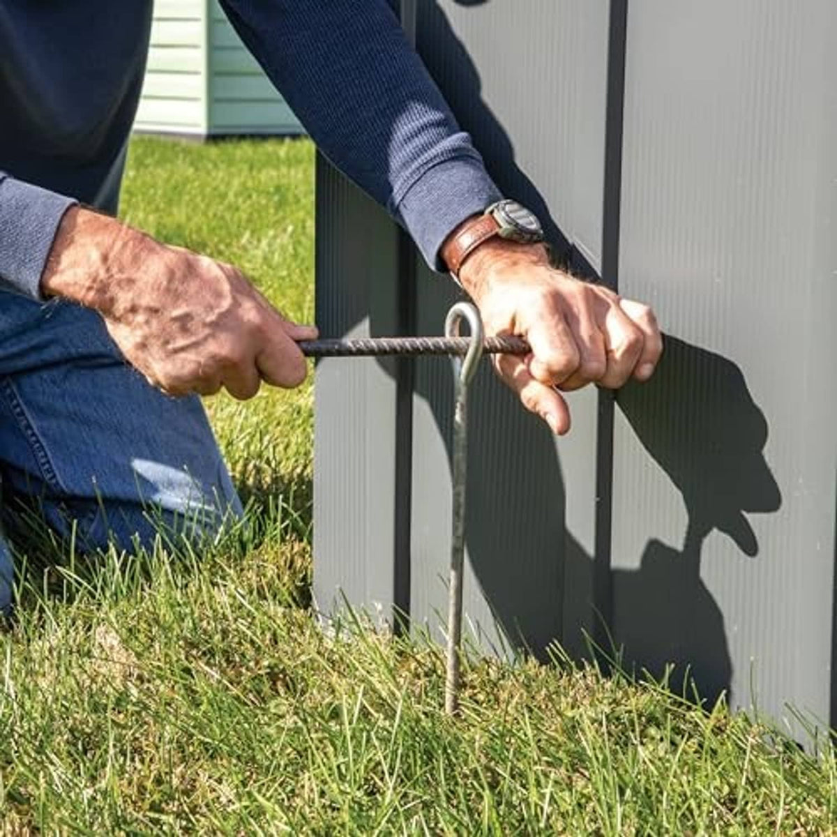 Hand installing a steel earth auger anchor into ground beside fence panel