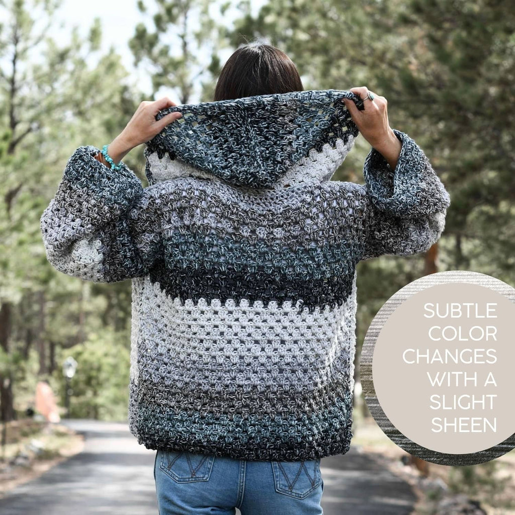Lion Brand Mandala Ombré yarn shown in a hooded crocheted sweater with gray and blue stripes