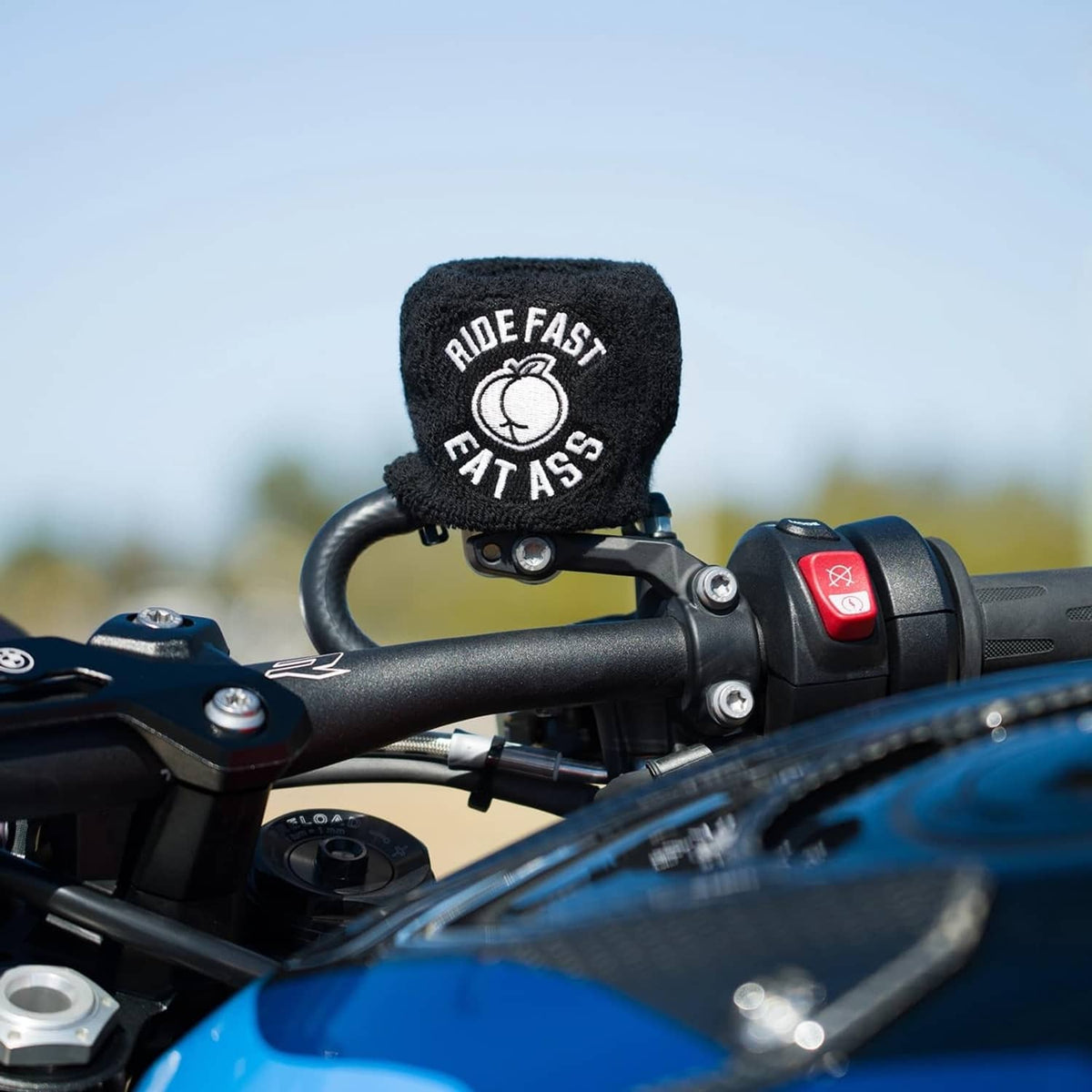 Black knit brake fluid reservoir cover sock with “RIDE FAST EAT ASS” logo, near switch