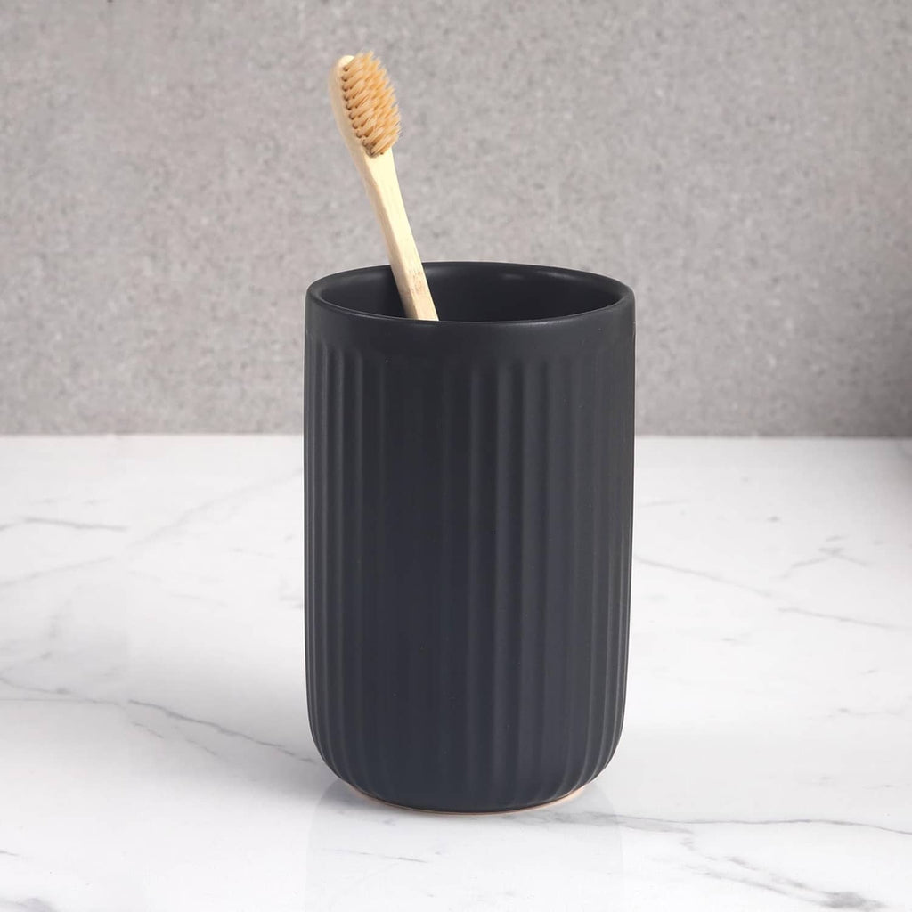 Matte black ceramic toothbrush holder cup with a ribbed side and upright toothbrush