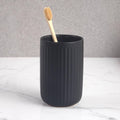 Matte black ceramic toothbrush holder cup with a ribbed side and upright toothbrush