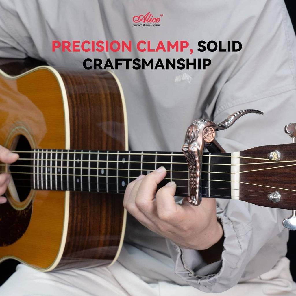 Bronze alligator-style guitar capo clamped on acoustic guitar neck, held by hand