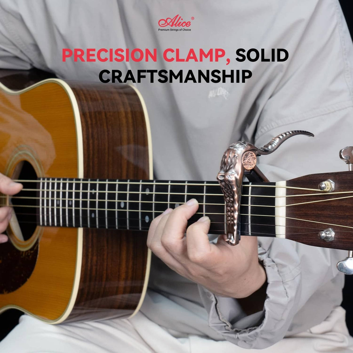 Bronze alligator-style guitar capo clamped on acoustic guitar neck, held by hand