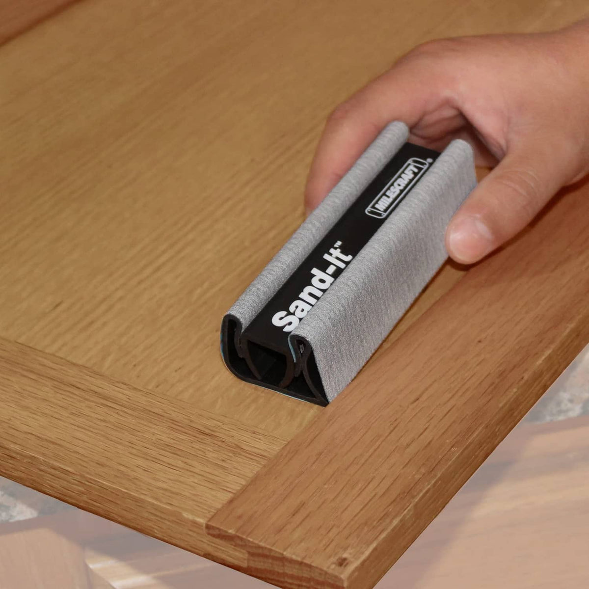 Milescraft Sand-It sanding block held on wood surface, gray sleeve with black U frame