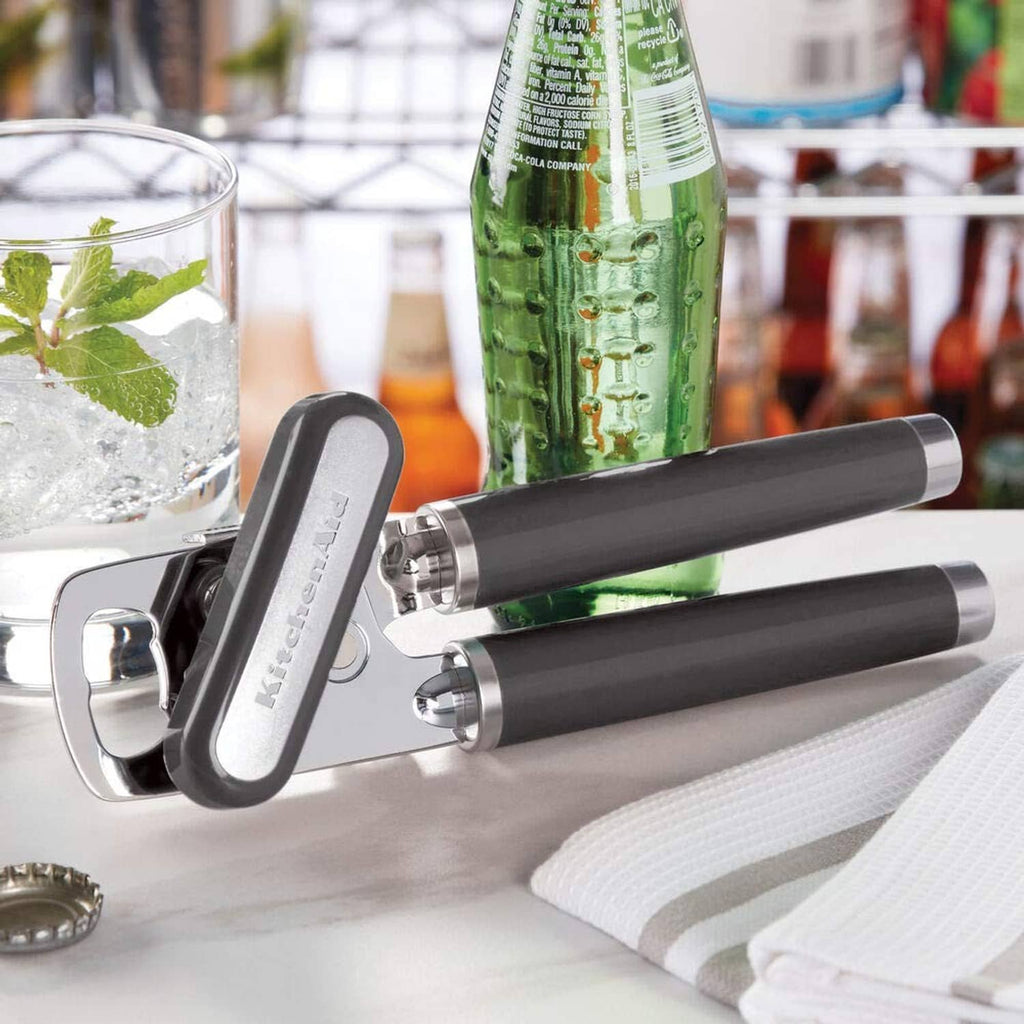 KitchenAid bottle opener with charcoal handle gripping bottle neck beside tray