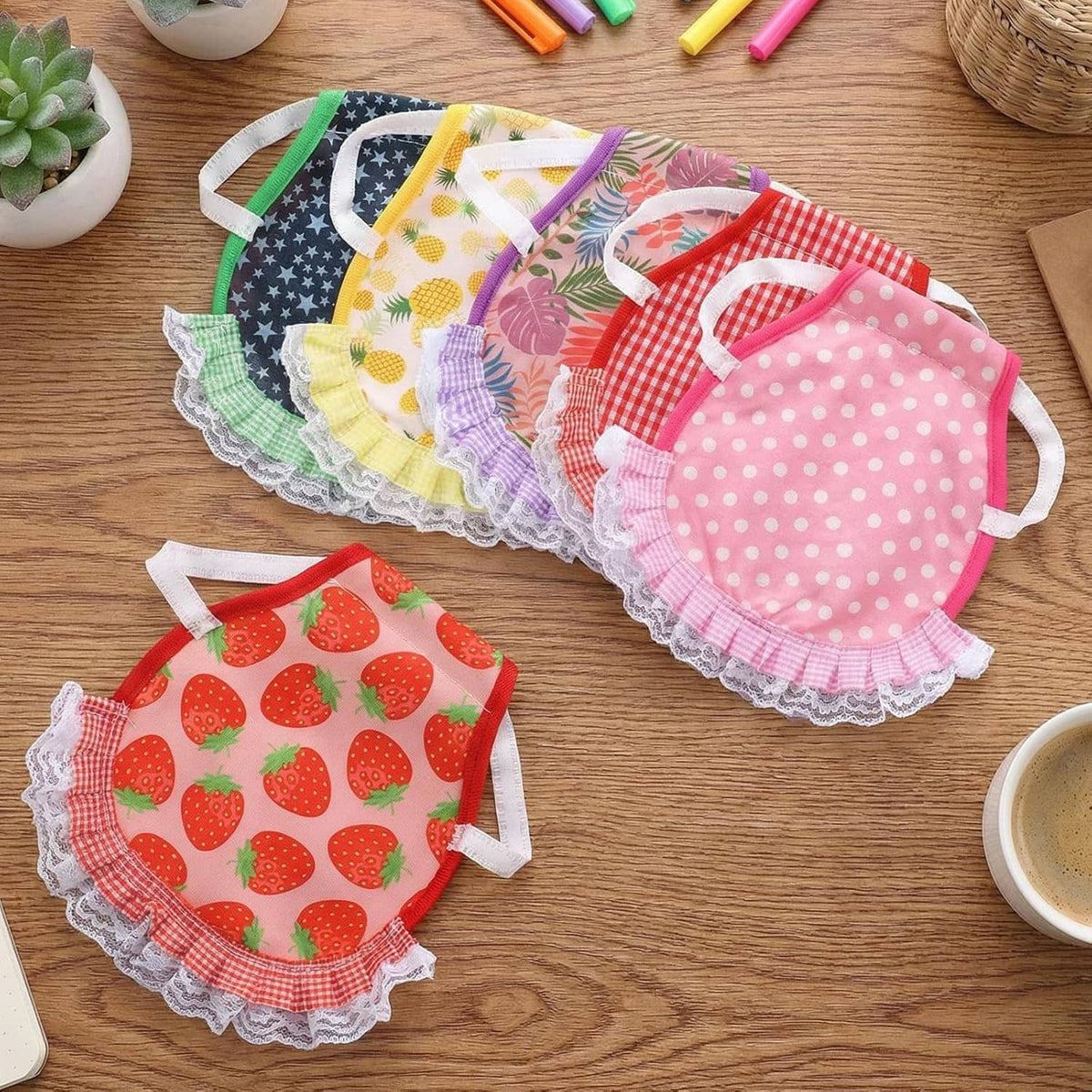 Assorted printed chicken saddle aprons with white lace trim laid on a wooden tabletop