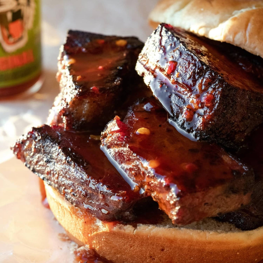 Hot sauce bottle near pulled ribs on buns with glossy red sauce topping