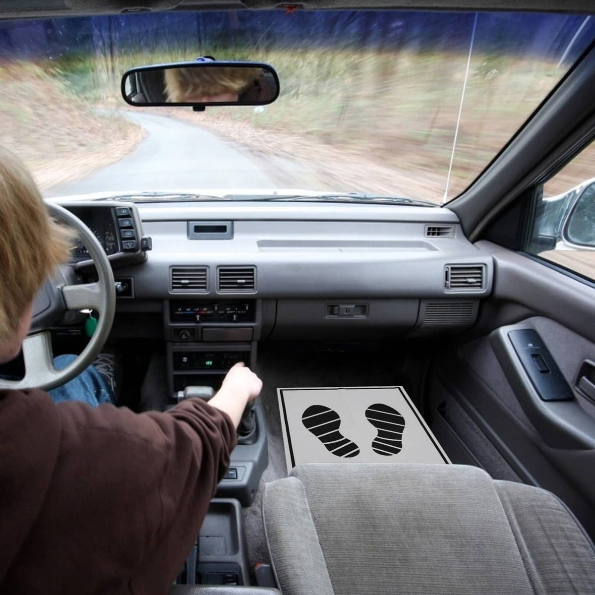 Disposable paper foot mat with black footprint print on driver-side car floor
