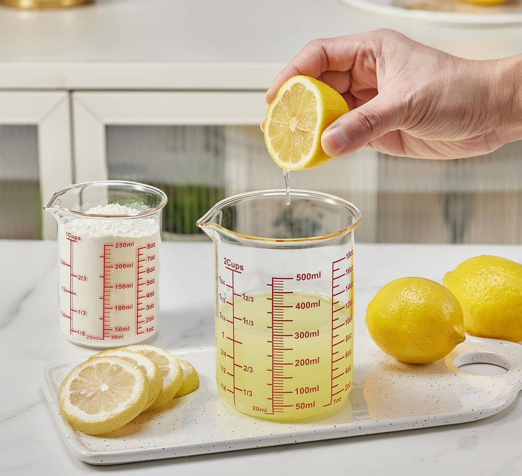 Clear glass measuring cup with red scale and V-shaped spout, pouring lemon juice