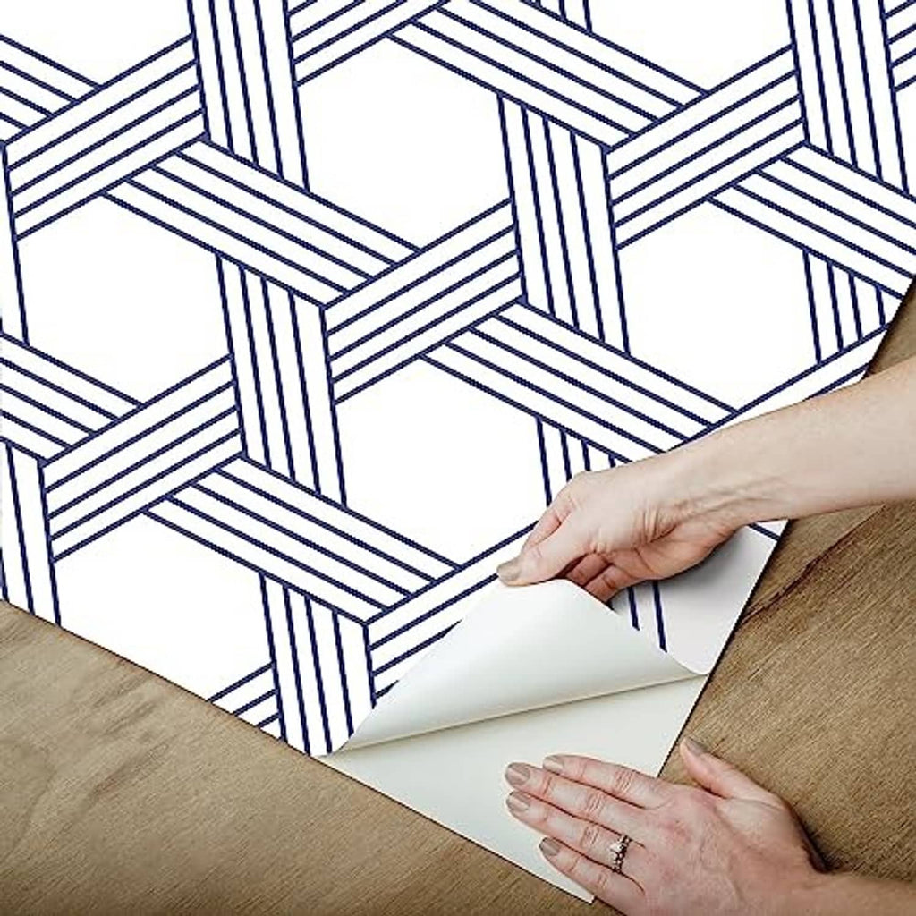 Hands applying a blue-and-white geometric lattice wallpaper sheet.