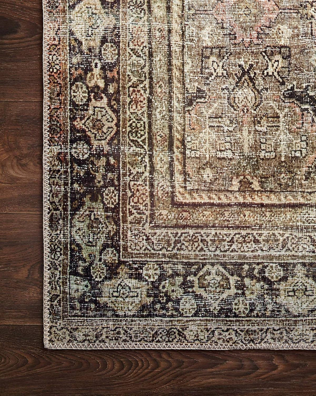 Vintage area rug corner detail with dense motifs and distressed olive, cream, and charcoal colors