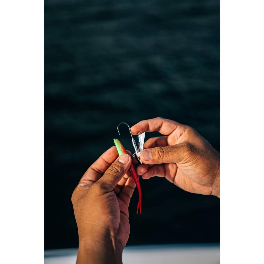 Close-up of a green soft plastic shad lure with red tail strands and exposed hook