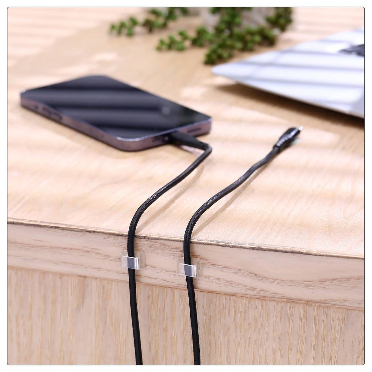 Clear adhesive clips holding black Christmas cords along a wooden surface.