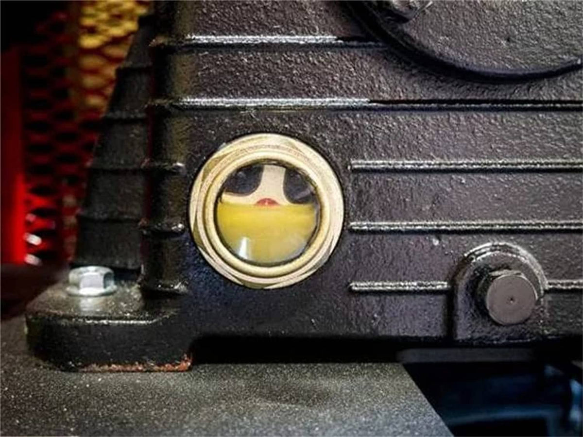 Close-up of compressor housing with small circular sight window showing yellow fluid and bezel