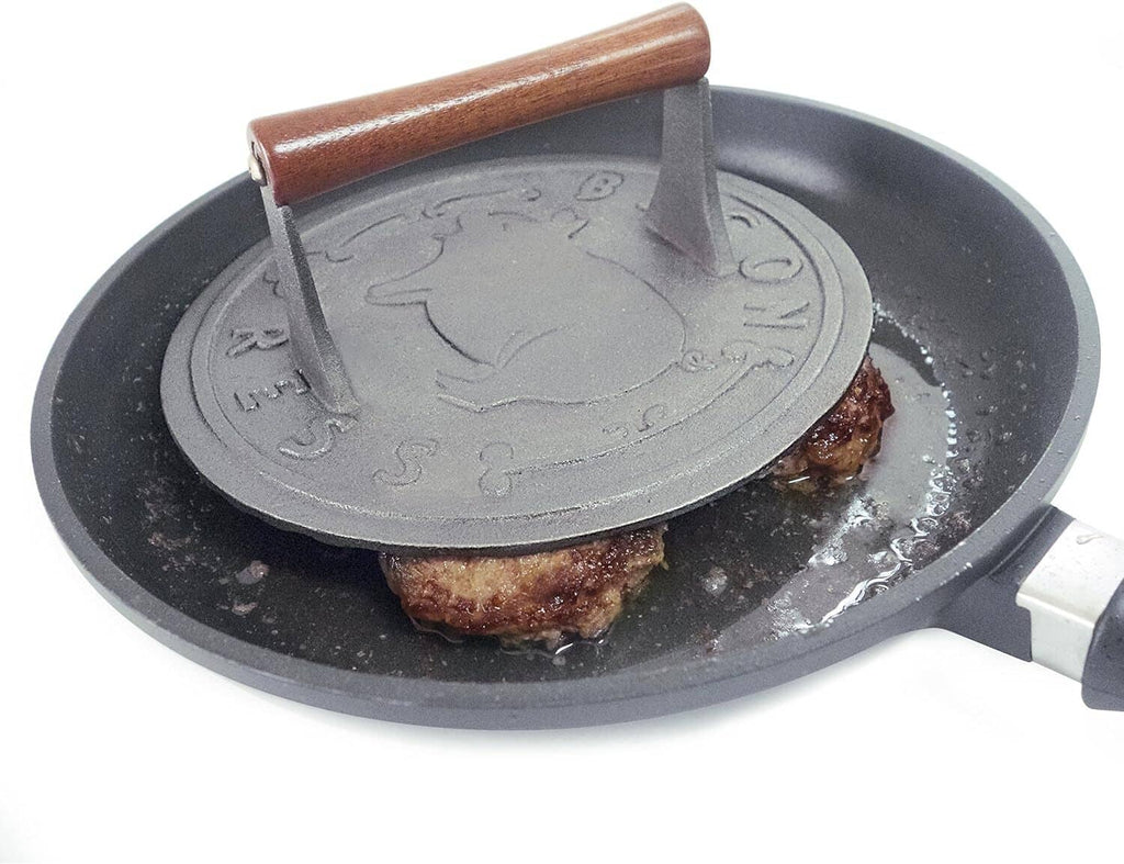 Cast iron bacon press with wooden handle compressing a piece of meat in pan