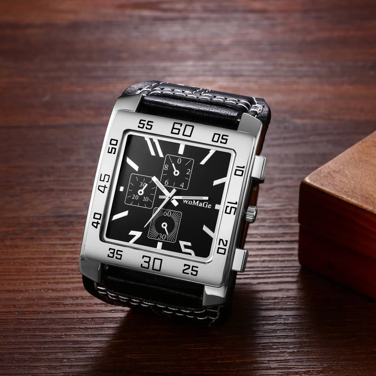 Square wristwatch with black dial, silver bezel, and black leather strap on wood surface