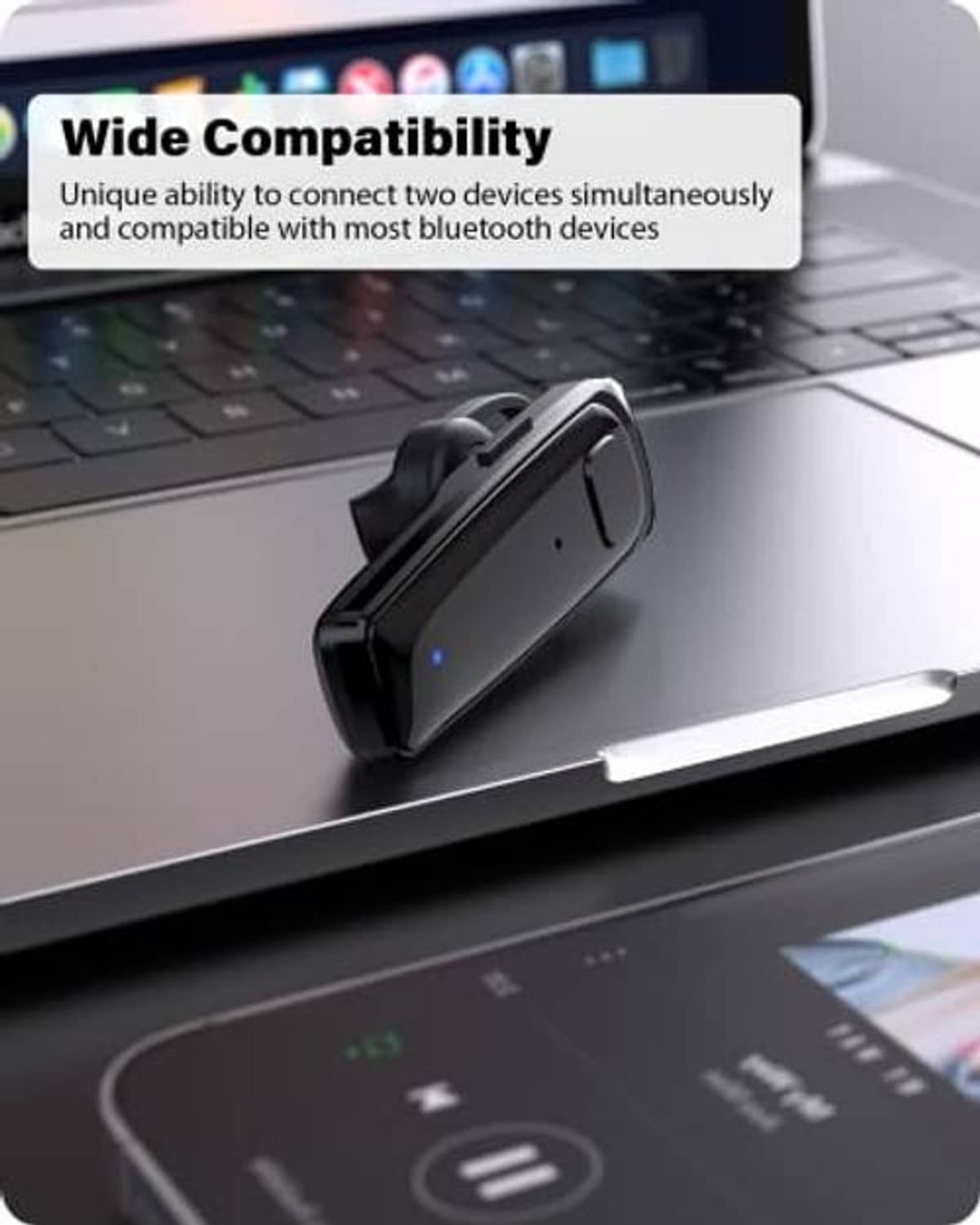 Black wireless headset resting on a desk near a laptop.