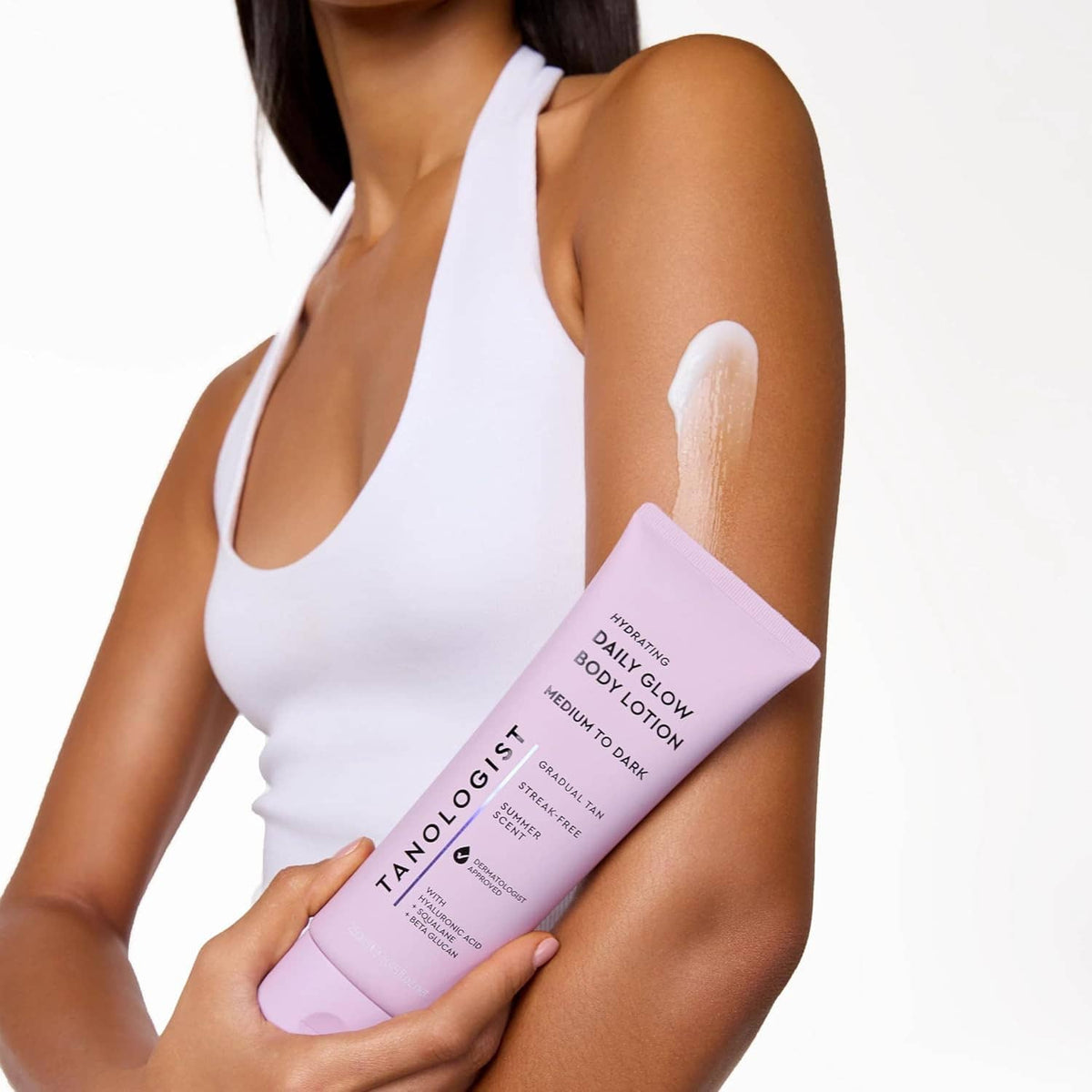 Woman holding lavender tanning body lotion tube while wearing a white tank top