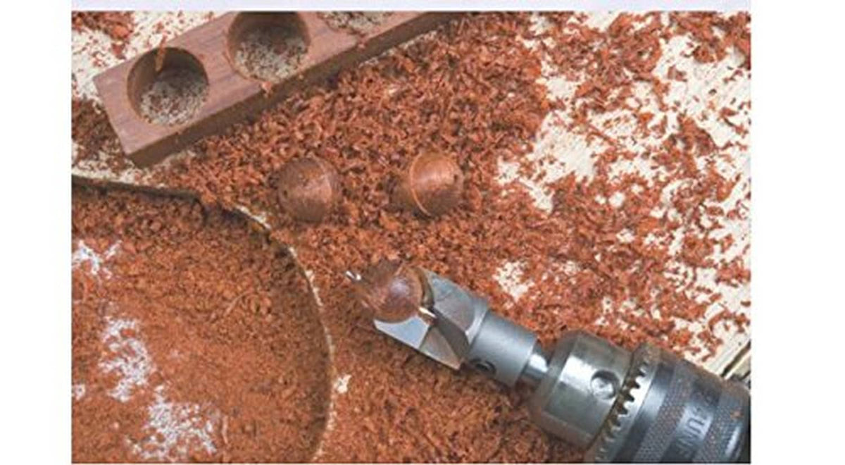 Wood carving hole cutter bit drilling into dark wood, metal shavings visible