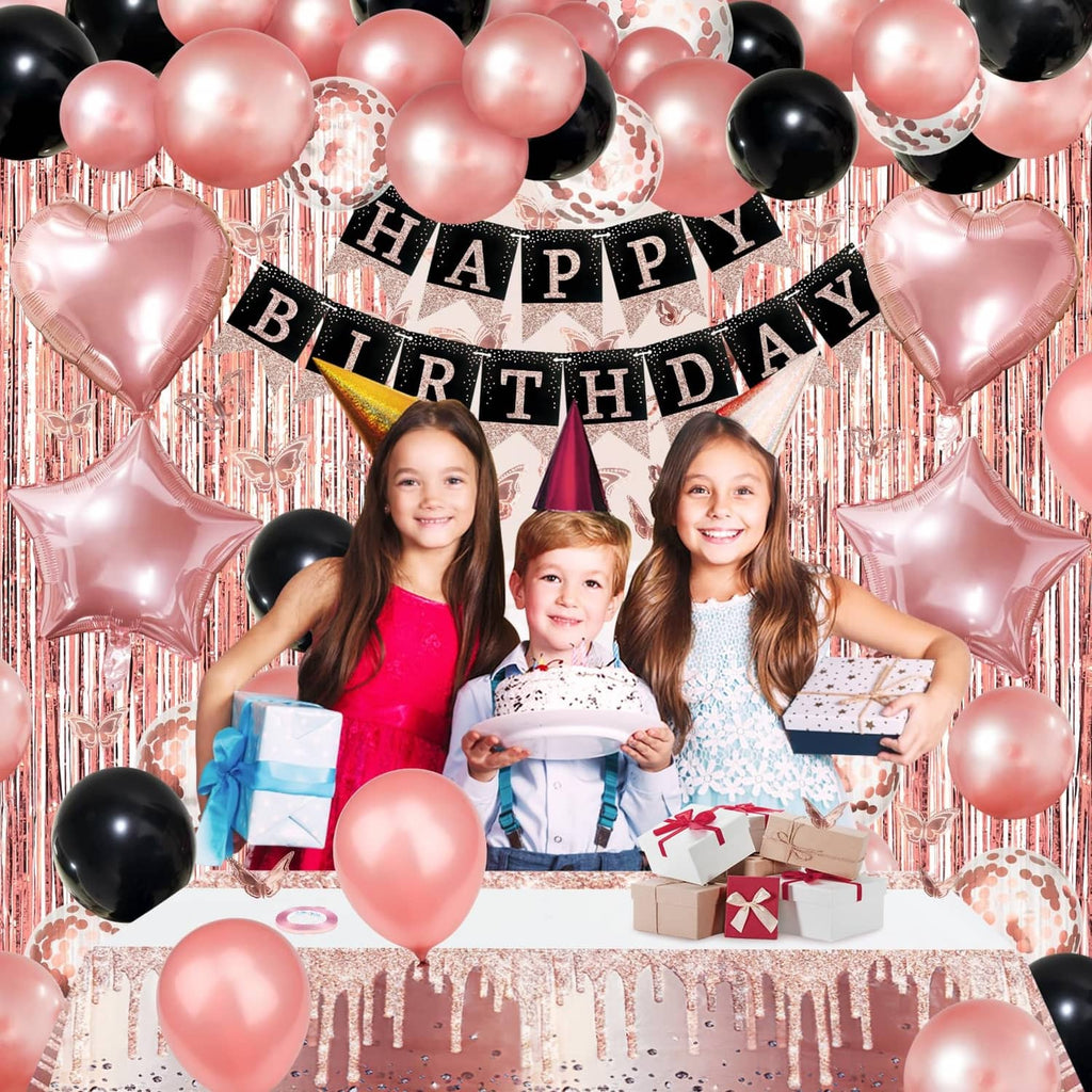 Happy Birthday banner with rose gold and black balloons framing a cake and gift table
