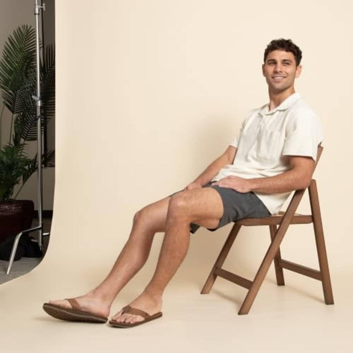Men's brown leather flip-flop sandals worn by a seated model, open-toe thong design