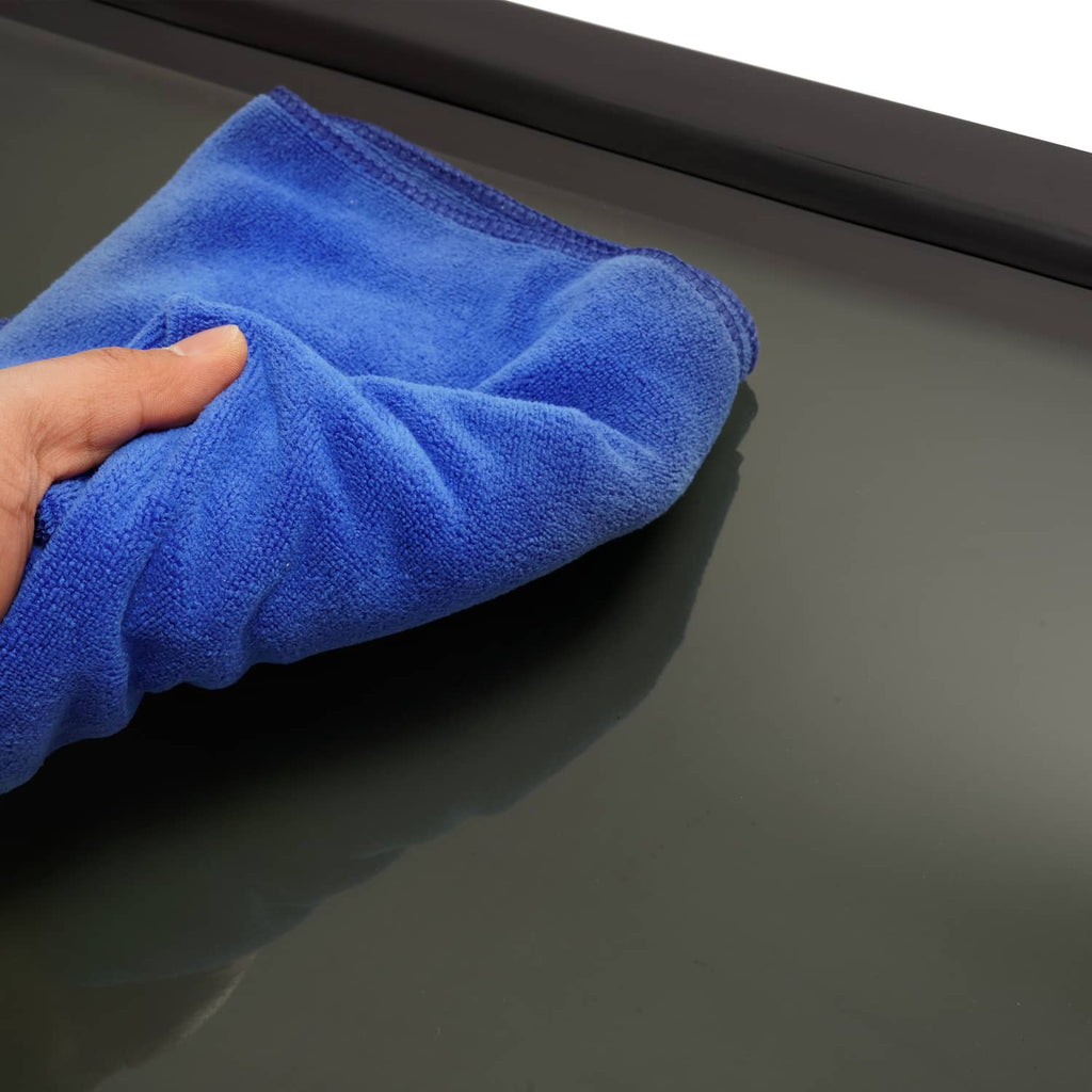 Hand wiping a tinted RV window panel with a blue microfiber cloth