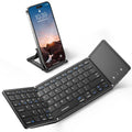 Foldable black Bluetooth keyboard with touchpad, angled open beside a phone stand
