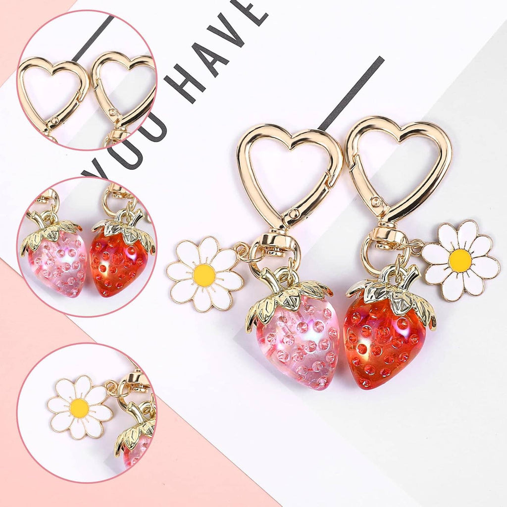 Two gold heart keychains with pink and red strawberry charms, daisies, and small leaf details