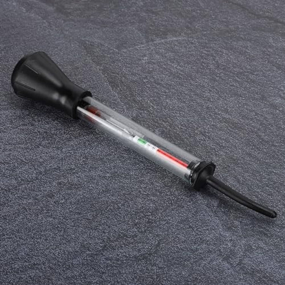 Battery hydrometer tester lying on textured surface, clear tube with red fluid indicator