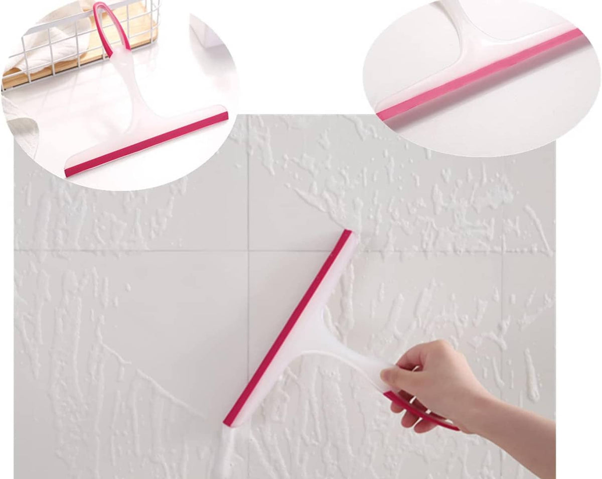 Hand using a pink silicone shower squeegee to wipe water from a tiled wall.