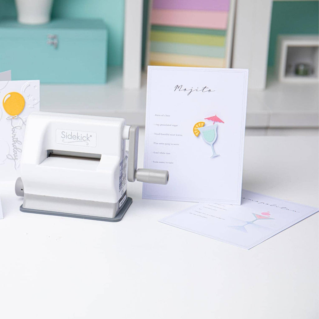 White die-cutting machine beside greeting card and teal cutting/embossing plate