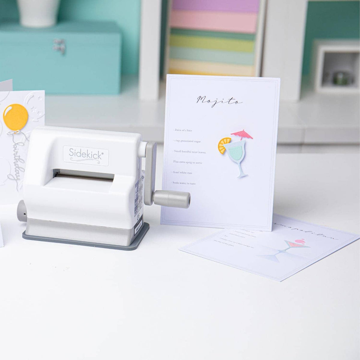 White die-cutting machine beside greeting card and teal cutting/embossing plate
