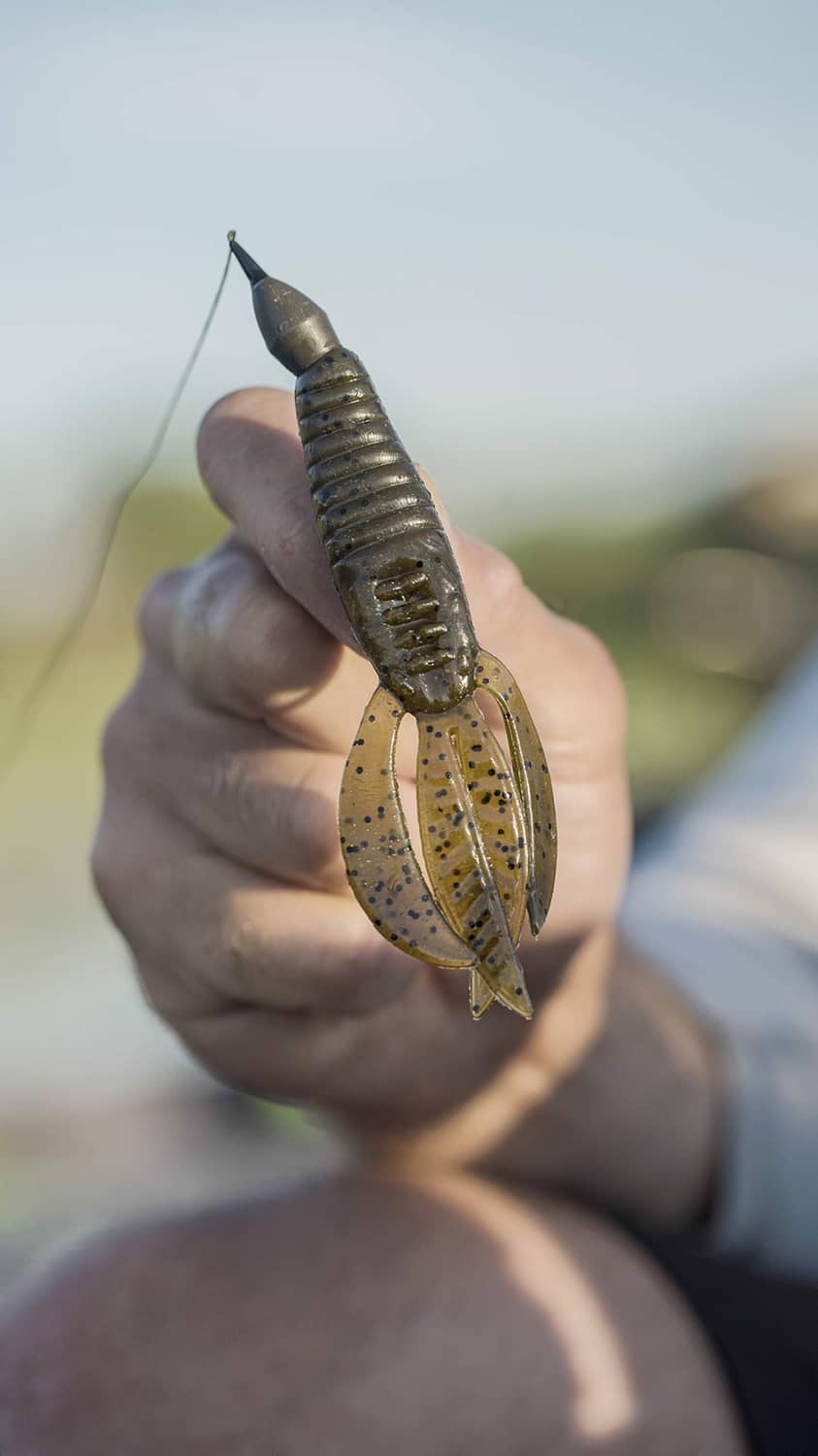 Fishing lure in hand, ribbed blue-green body and yellow-orange speckled tail