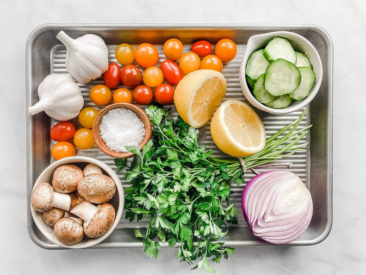 Quarter sheet pan filled with vegetables, herbs, garlic, and lemon halves