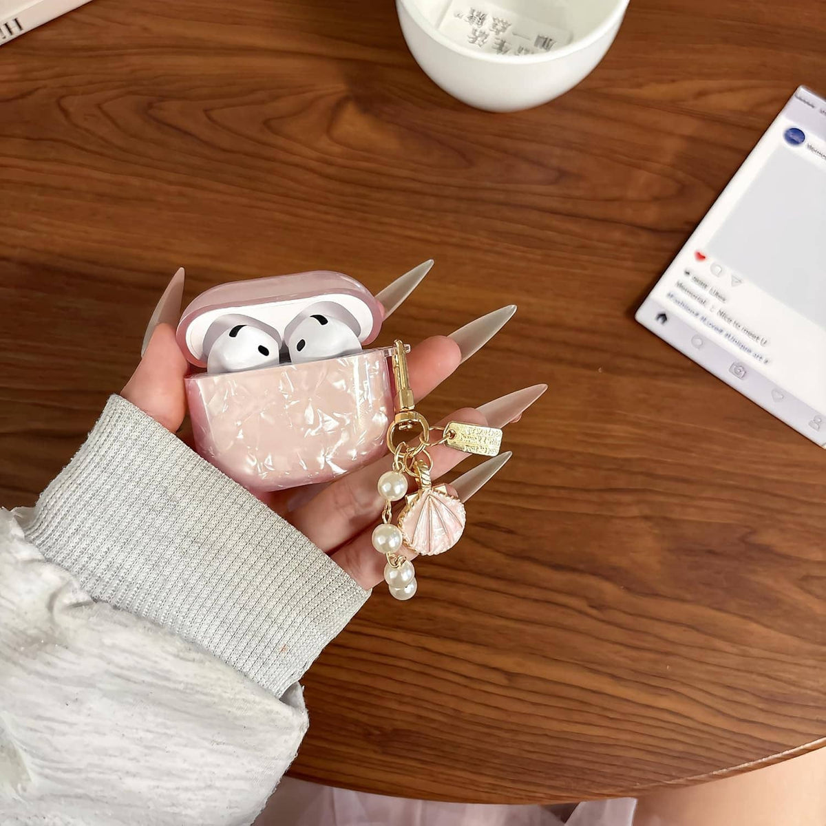 Pink glitter TPU AirPods case with pearl keychain charm, earbuds inside held in hand