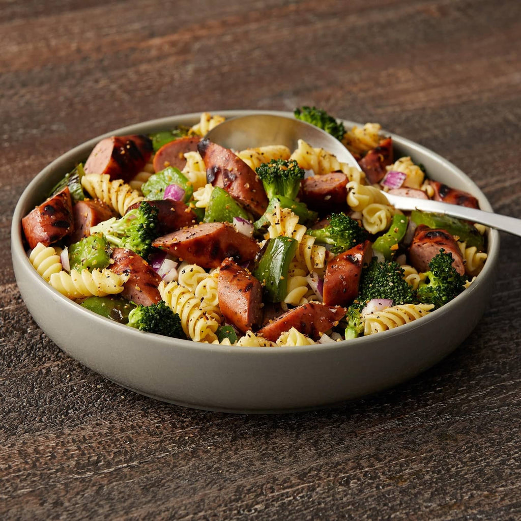 Bowl of rotini pasta with meat pieces, broccoli, and seasoning