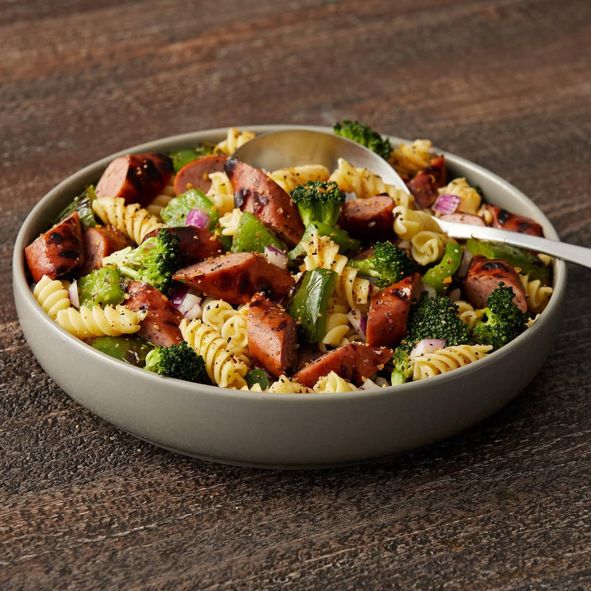 Bowl of rotini pasta with meat pieces, broccoli, and seasoning