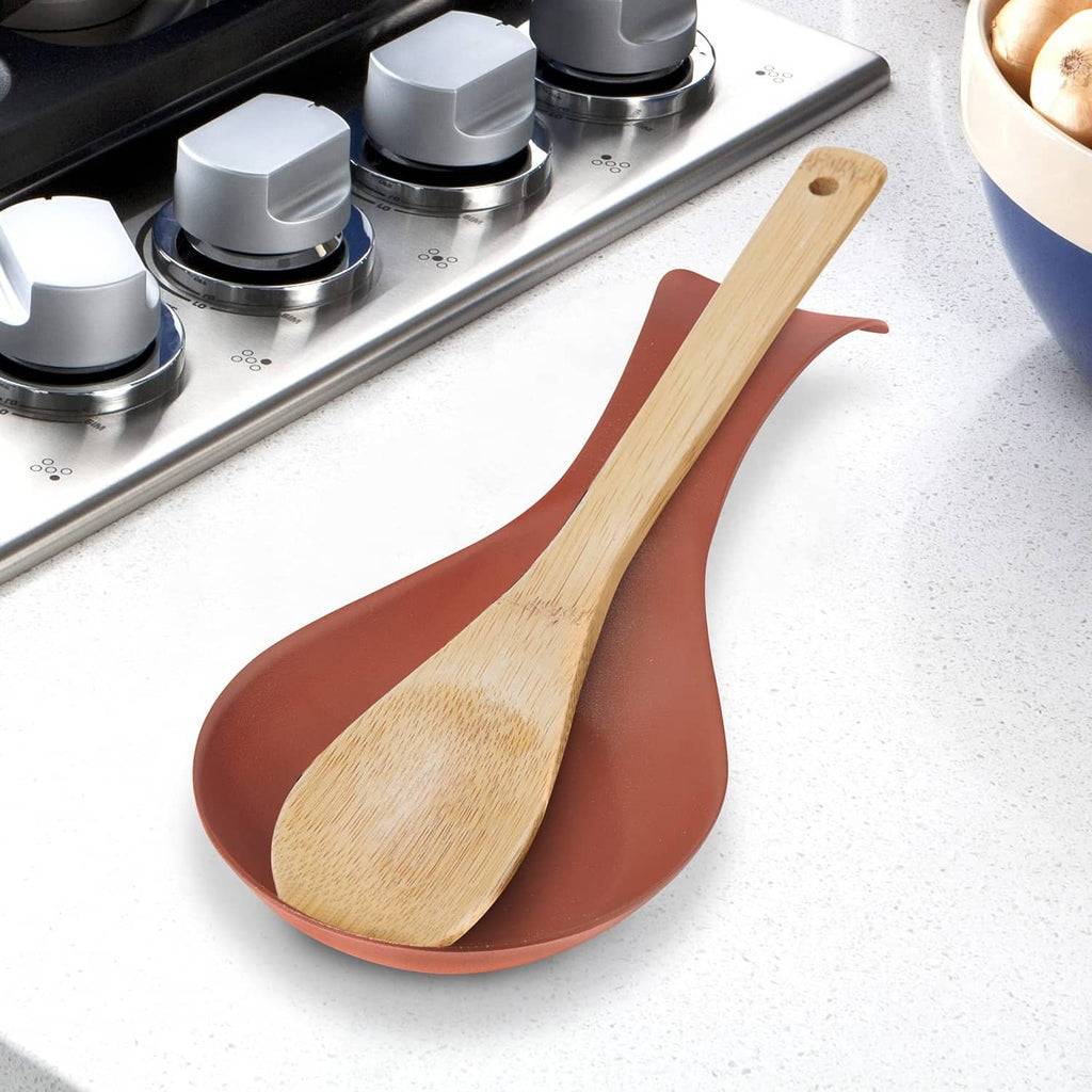 Brick-red stainless spoon rest on a counter with a wood spoon resting in the bowl
