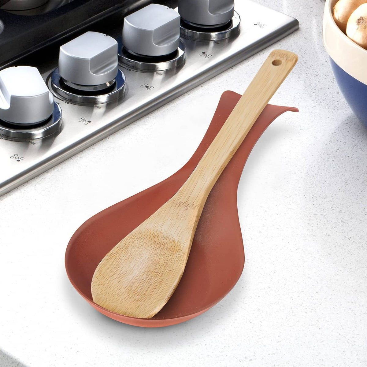 Brick-red stainless spoon rest on a counter with a wood spoon resting in the bowl