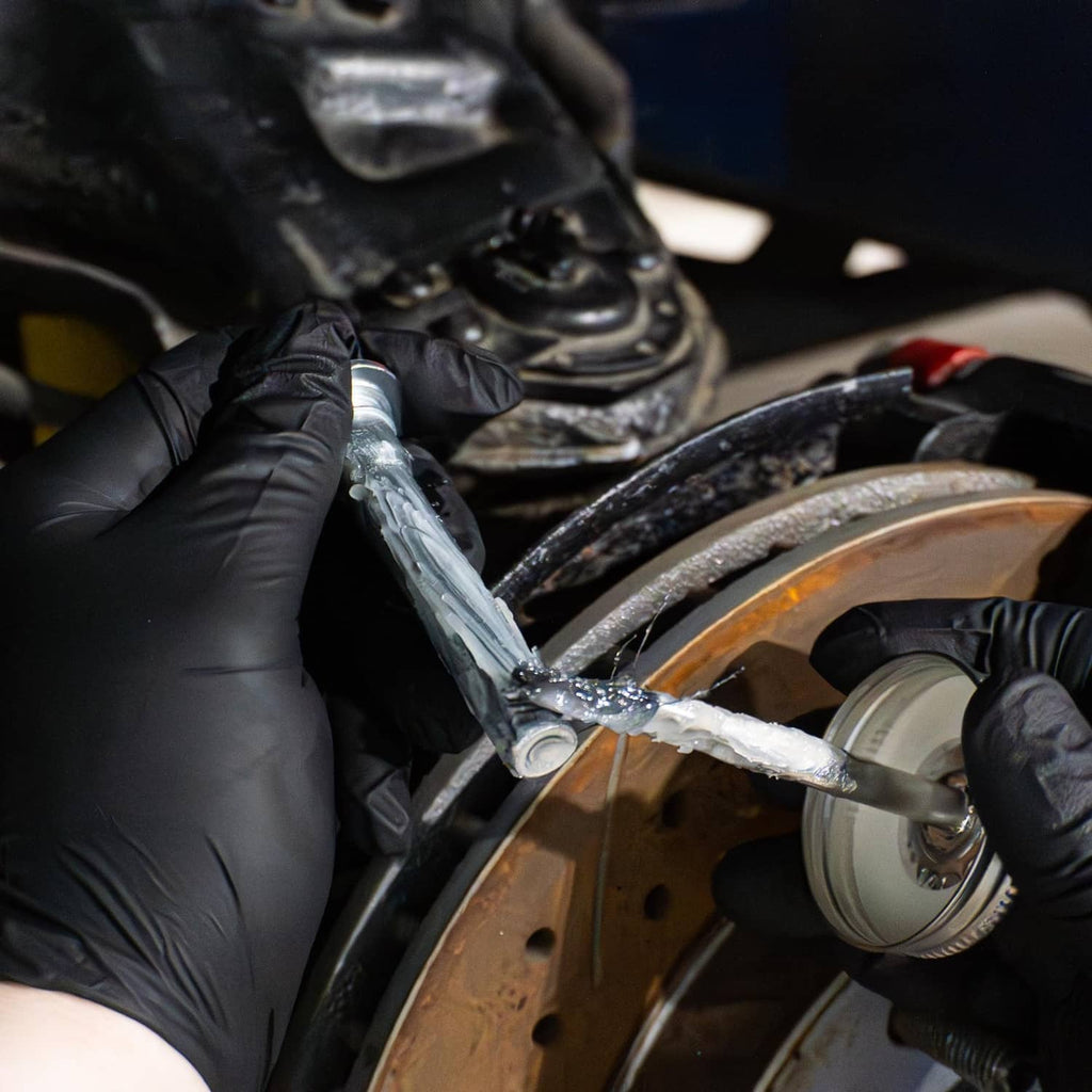 Gloved hands apply silicone brake lubricant with brush to brake part