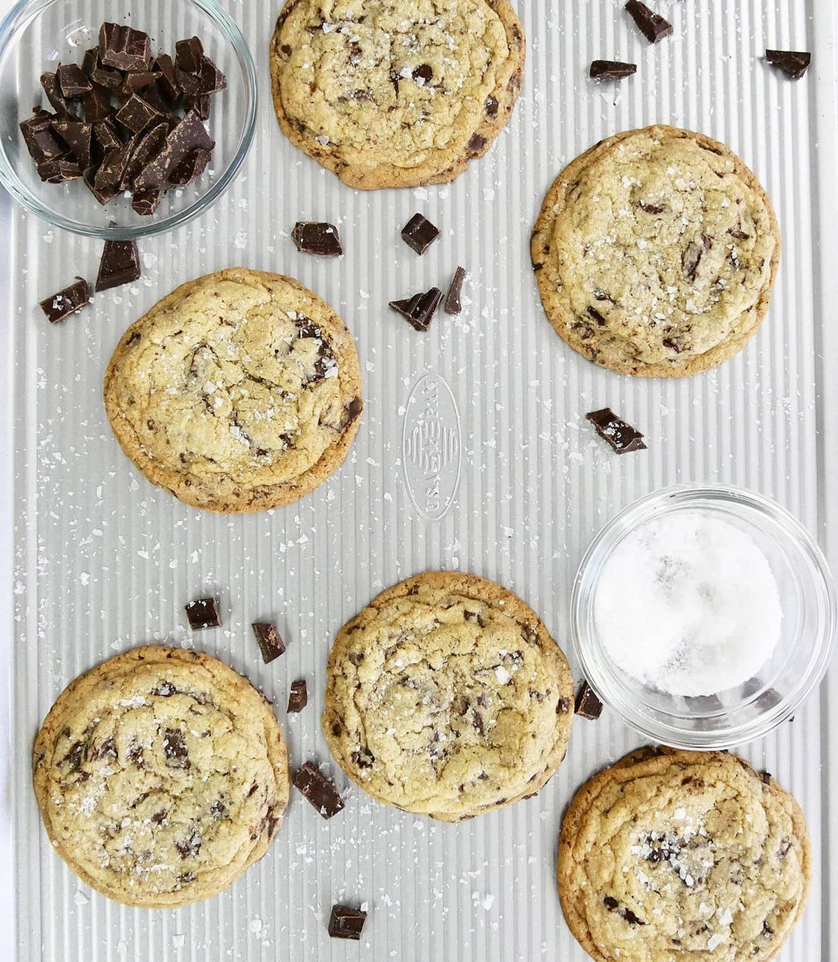 Nonstick cookie sheet with baked chocolate chunk cookies and scattered chocolate pieces