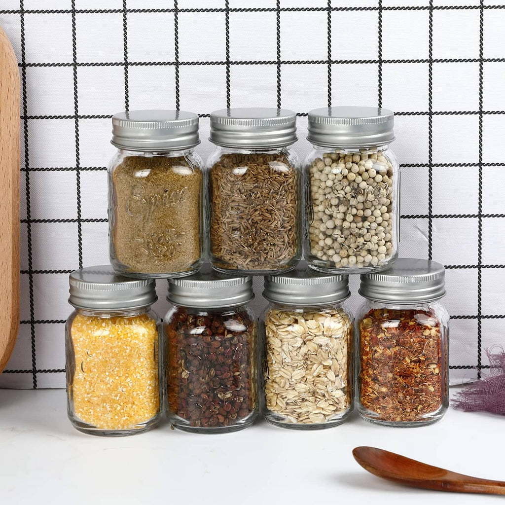 Set of clear round glass spice jars with silver lids, filled with assorted seasonings