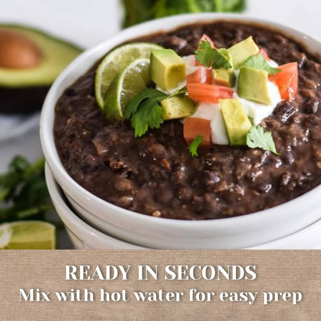 Dark veggie soup in bowl topped with lime wedges, avocado cubes, and cilantro