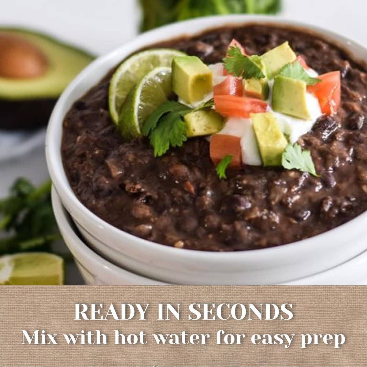 Dark veggie soup in bowl topped with lime wedges, avocado cubes, and cilantro