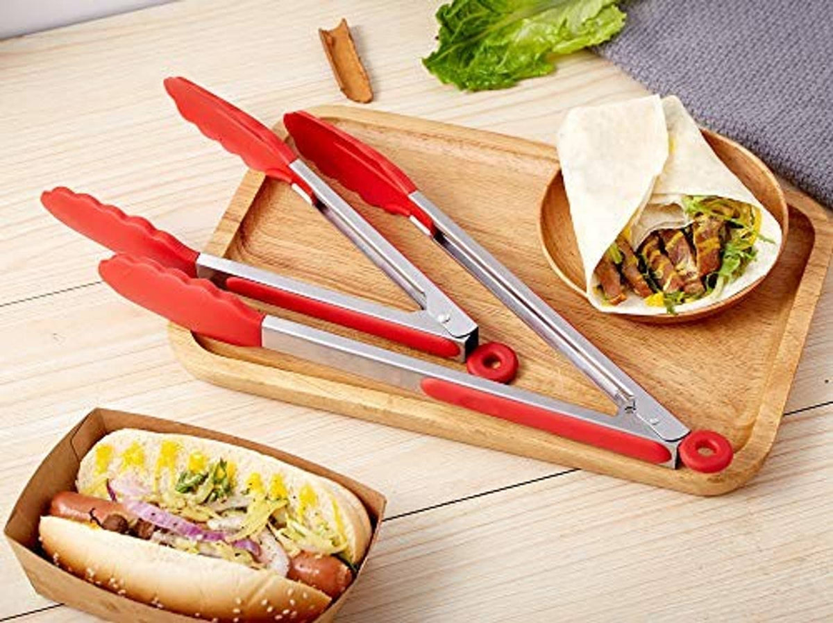 Pair of red silicone-handled stainless steel kitchen tongs on a wooden tray.