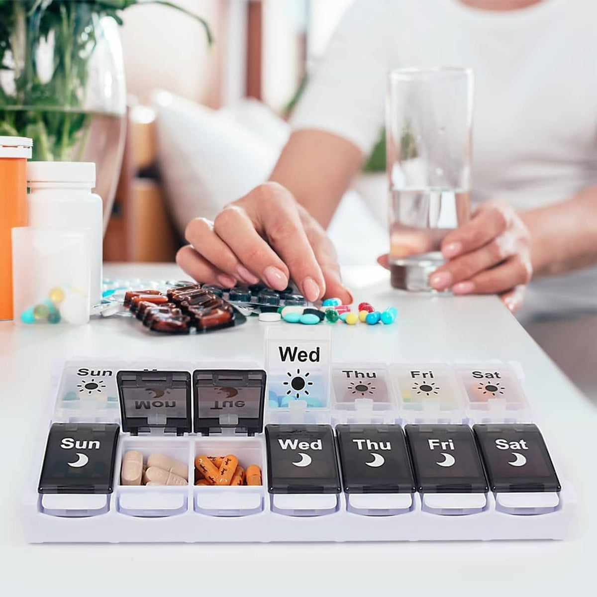 Weekly pill organizer on table with hand placing pills into Sun-Sat compartments