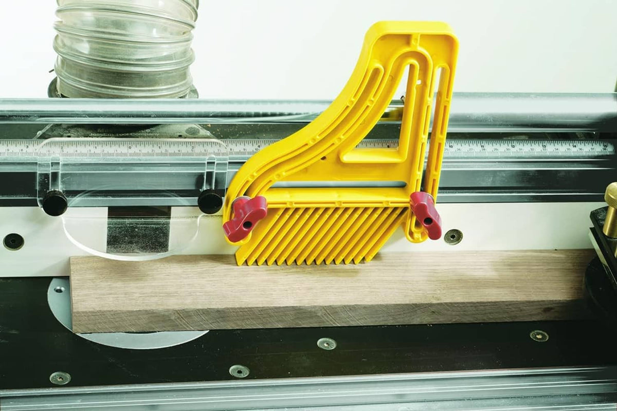 Yellow featherboard with red clamps mounted on a router table for woodworking