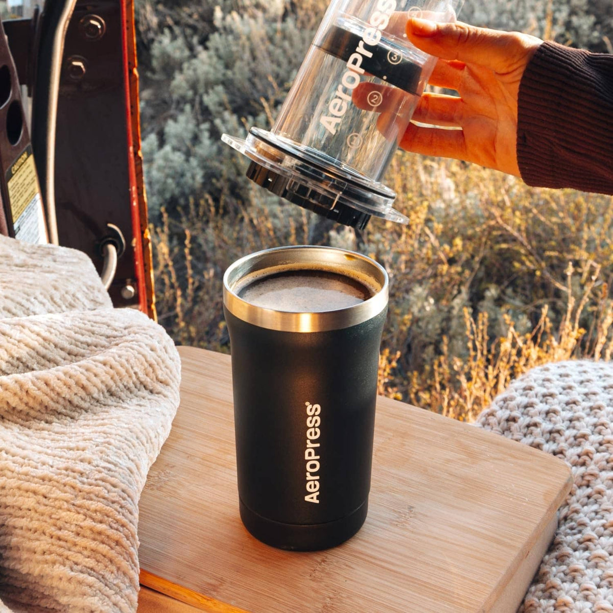 Portable black AeroPress coffee maker on table with metal cup filled with coffee.