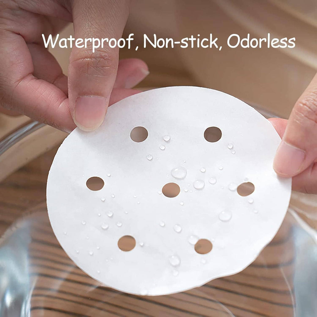 Hands holding a round perforated white steamer liner pad with water droplets